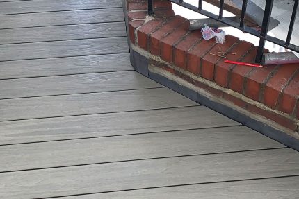 Curved brickwork and precision metal flashing bordering modern composite decking on a high end London balcony renovation.