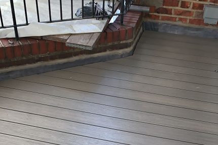 Grey composite decking intersecting with a traditional brick wall and precision flashing trim on a luxury balcony.