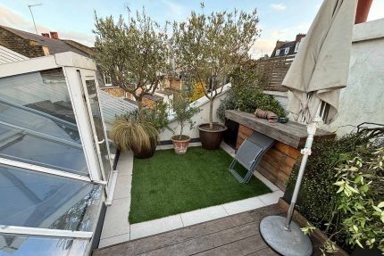 Seamless integration of wooden decking, stone tiles, and artificial grass on a fully naturalised London roof terrace.