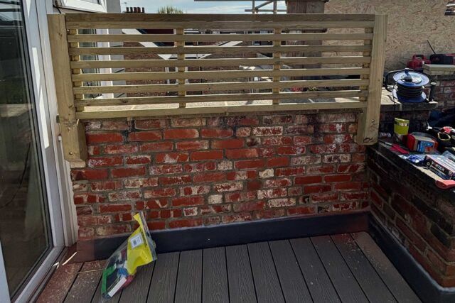 Bespoke timber privacy screen complementing rustic brickwork and grey eco-friendly decking on a luxury roofer London installation.