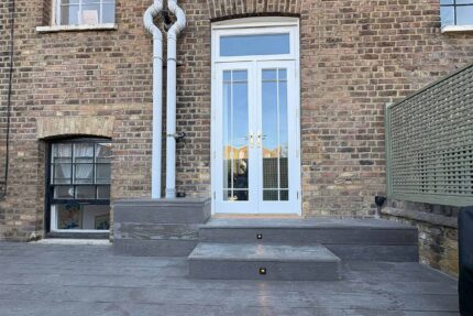 Grey composite decking steps seamlessly connect elegant French doors to the newly restructured Little Venice roof terrace, showcasing premium London roofing finishes and significant property value enhancement by our expert contractor team.