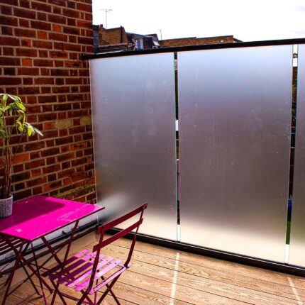 Frosted glass roof balustrade and privacy screen installed on a wooden decked roof terrace with pink outdoor seating.