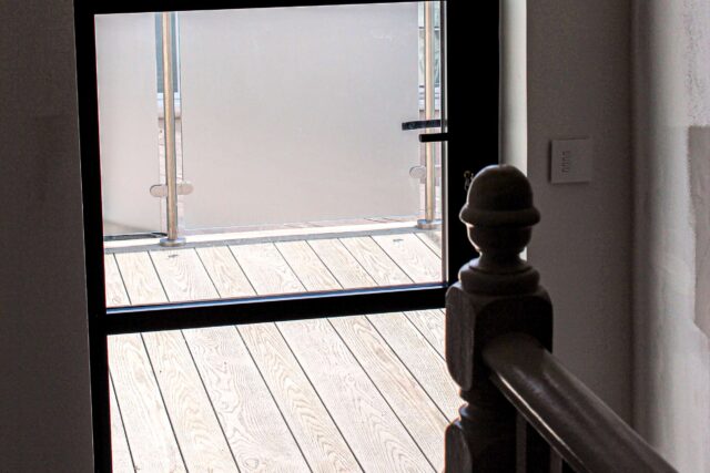 Weather-resistant composite decking sitting securely behind a frosted glass privacy balustrade on a bespoke flat roof terrace built by our roofer London team.