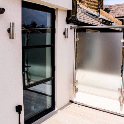 A newly installed frosted glass balustrade alongside a modern black framed door on a completed Vauxhall roof terrace featuring composite decking.