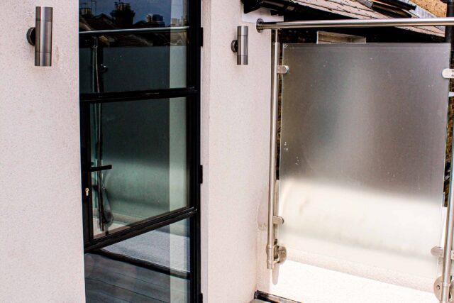 Frosted glass privacy balustrades and modern black framed aluminium access doors define this premium flat roofing London conversion in Vauxhall.