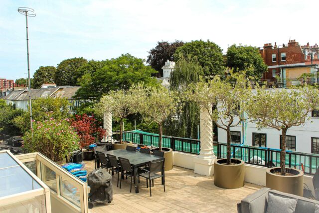 Eco-friendly timber composite decking frames an elegant outdoor dining area and bespoke planters on this luxury flat roofing London transformation in Holland Park.