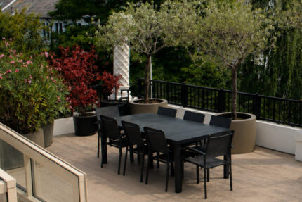 An outdoor dining area on a roof terrace featuring natural wood decking and a flat glass skylight.