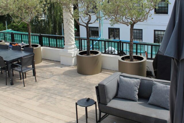 A sophisticated rooftop dining and lounge area featuring weather resistant timber decking and custom architectural planters overlooking West London.